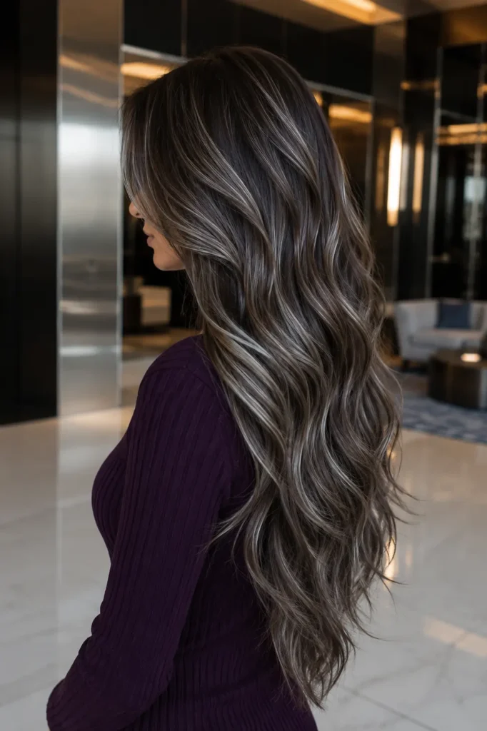 a white woman with extremely long ash brown hair featuring delicate silver highlights, cool smoky brunette tones, luminous metallic ribbons, loose waves, and layered ends, wearing a deep plum high-neck sweater in a sleek contemporary hotel lobby.
