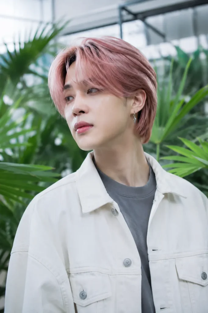 a young man with a Jimin-inspired dusty rose pink Korean hairstyle featuring layered medium-length hair and a soft centre-parted fringe, wearing a white denim jacket
