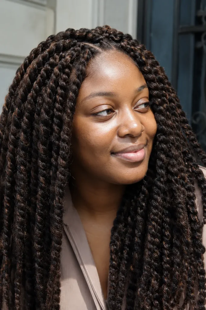 a Black woman wearing voluminous warm brunette Marley twist braids in bright natural daylight, showcasing realistic skin texture and a full, textured protective hairstyle against a soft neutral background.