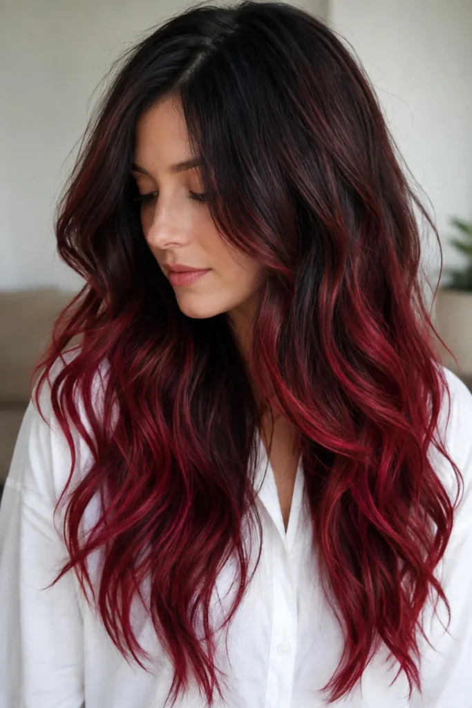 Cherry red ombré on very long wavy brunette hair with glossy ruby-red ends, photographed indoors on a woman wearing a white shirt.