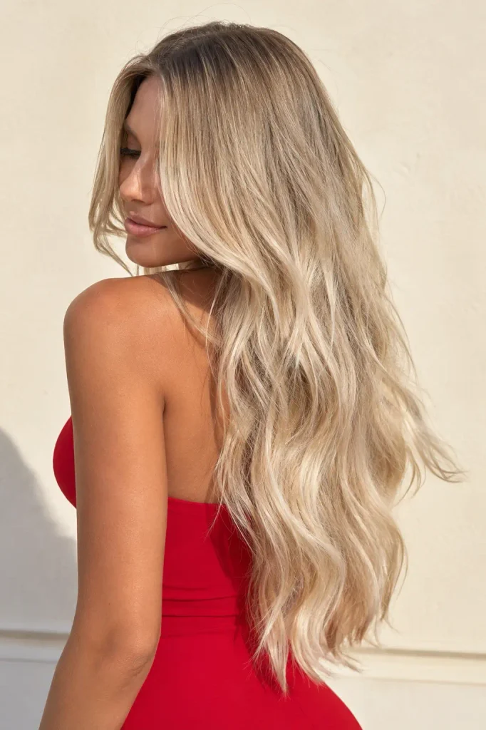 Photorealistic woman with extremely long creamy blonde balayage hair in soft flowing waves, wearing a fitted red dress against a minimal cream background.