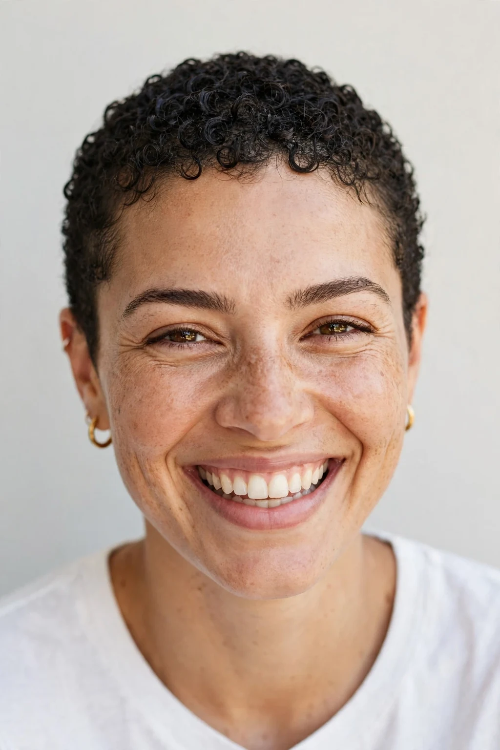 Woman with curly buzz cut, short defined curls, joyful bright light.