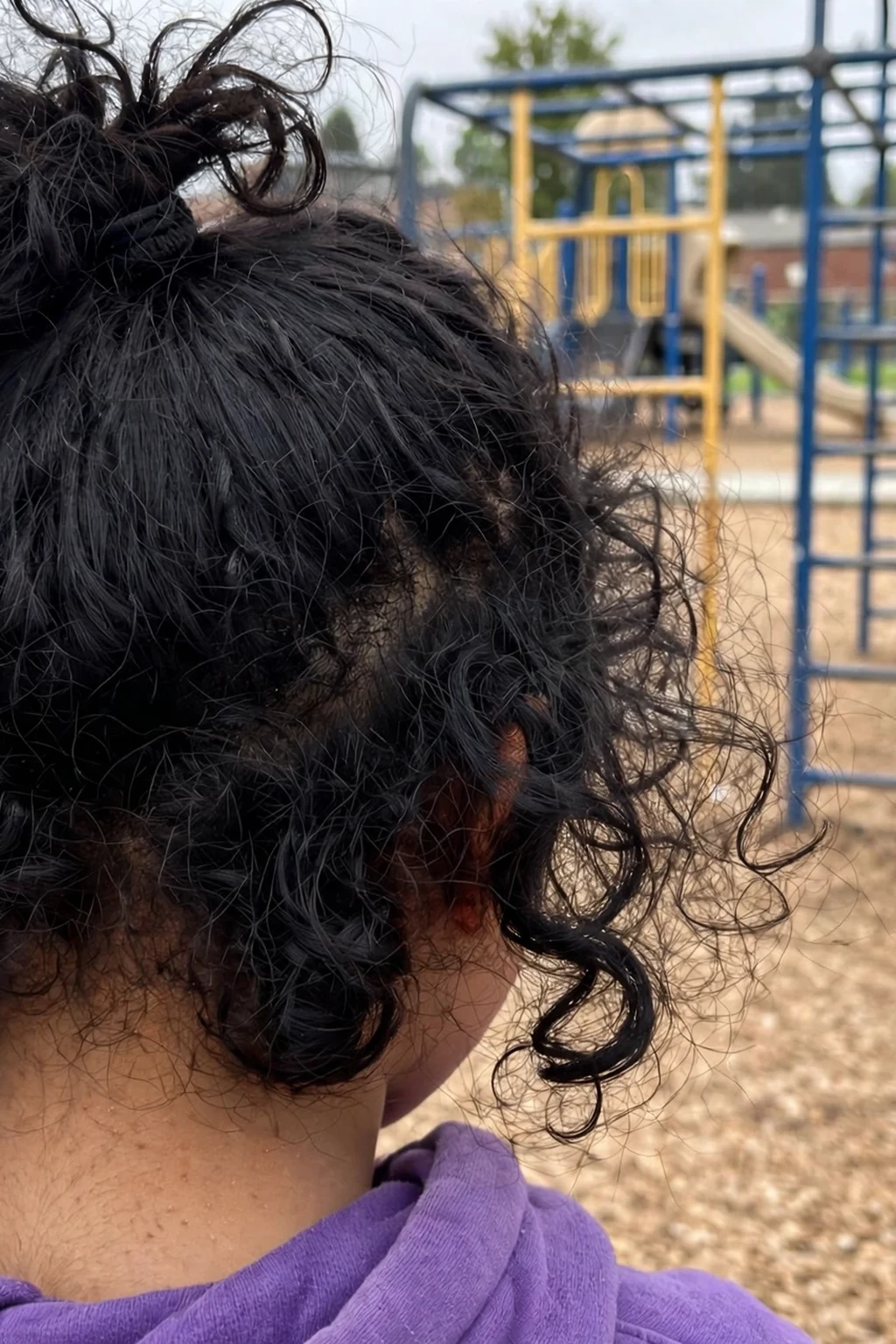 A young girl with curly hair in a half-up top knot, playing in a school playground.